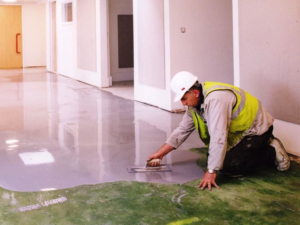 Процесс выравнивания бетонной стяжки алюминиевым правилом по металлическим маякам